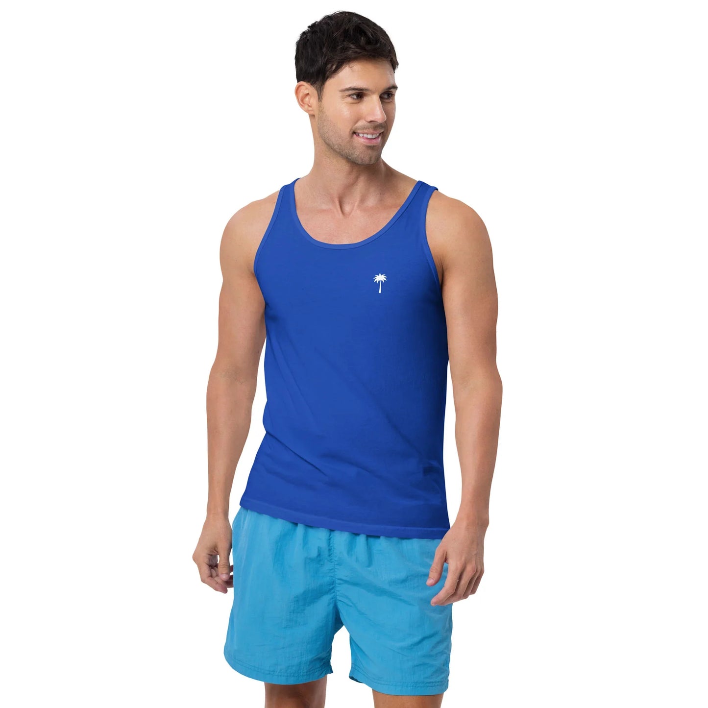 A man wearing a classic tank top with a small white palm tree graphic on the chest and light blue shorts stands smiling and looking to his left against a plain white background.