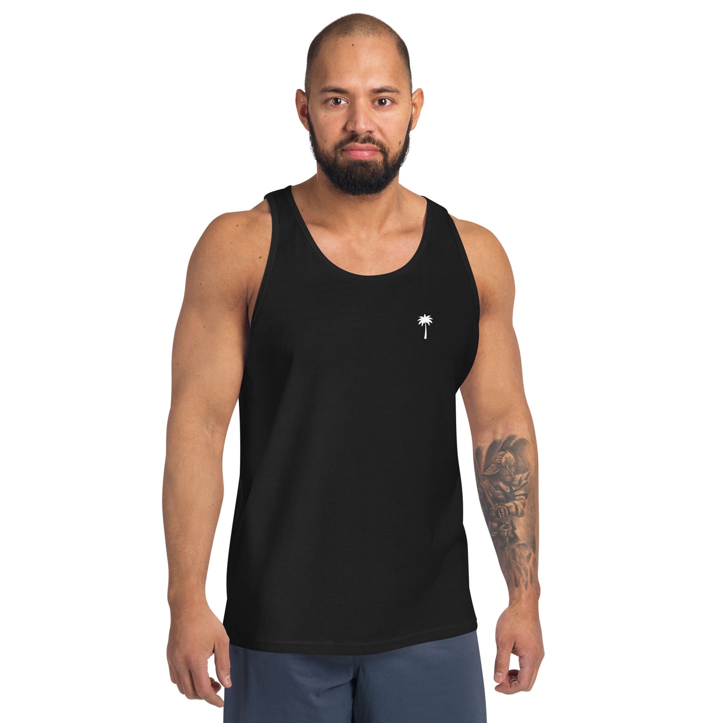 A man with a beard and a tattooed right arm wears a classic tank top made from soft ringspun cotton, featuring a small white palm tree design on the chest, standing against a white background.