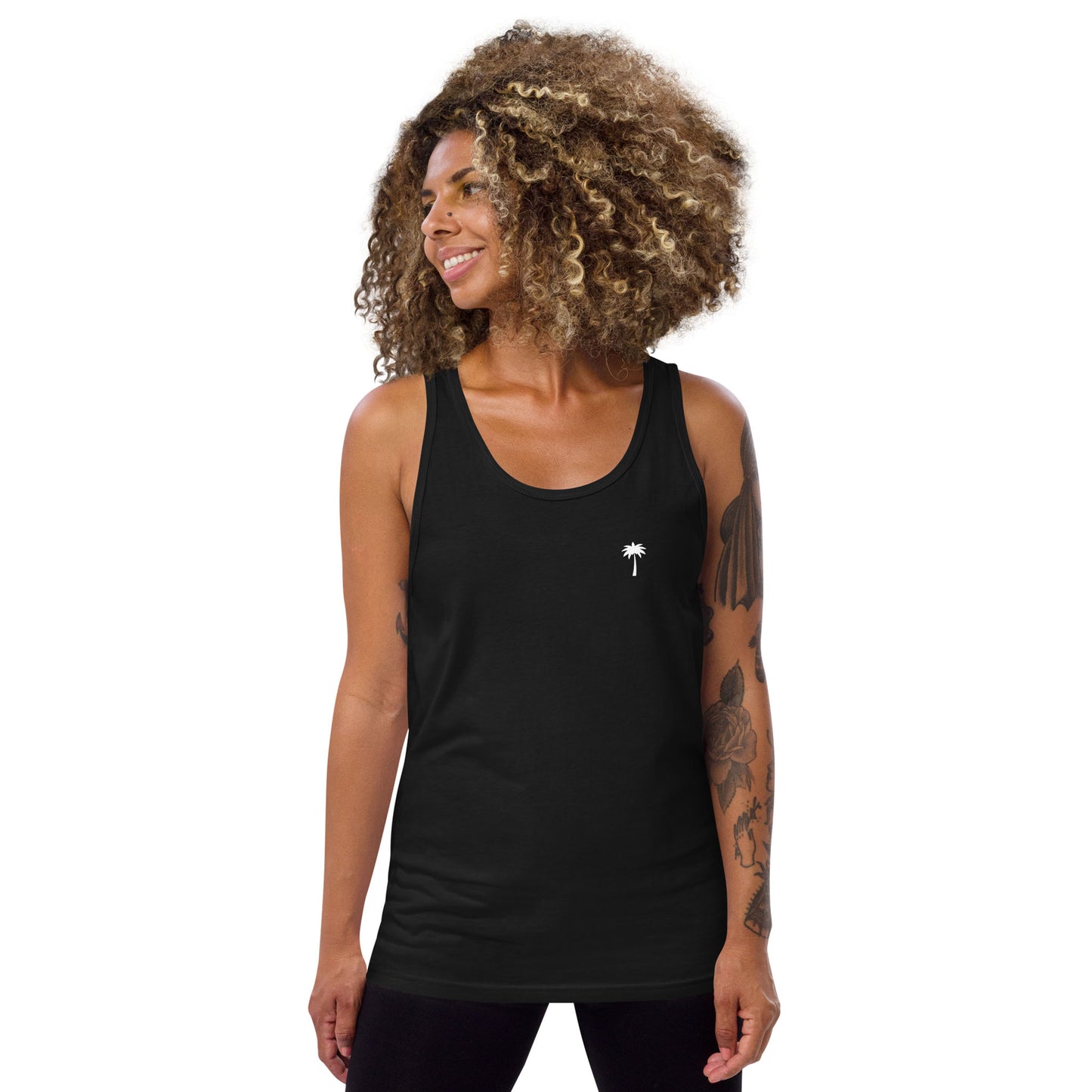 A woman with curly hair wears a classic tank top made from soft ringspun cotton, featuring a small white palm tree graphic on the left side. She smiles and looks to her left against a plain white background.