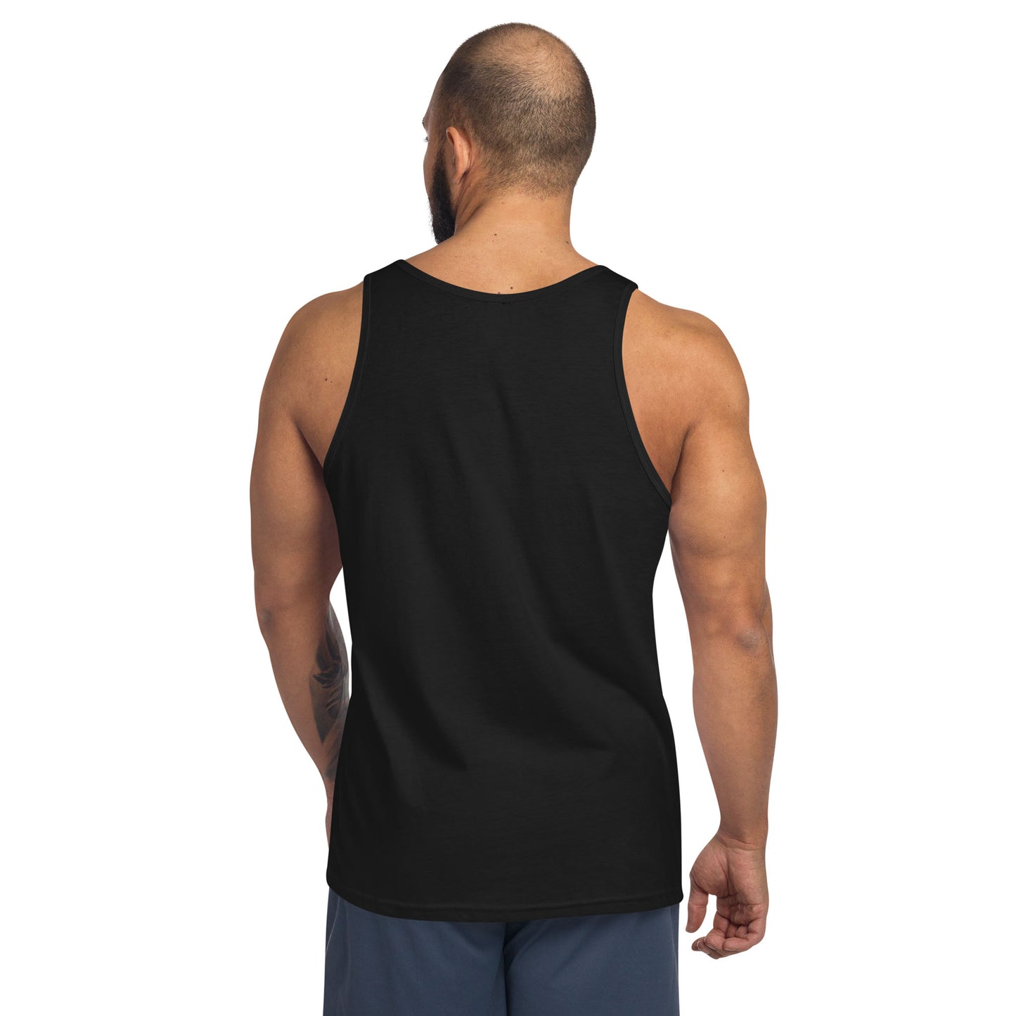 A man with a shaved head and beard is shown from behind, wearing a classic black tank top made of ringspun cotton and dark shorts. His right arm features a tattoo as he stands against a plain white background.