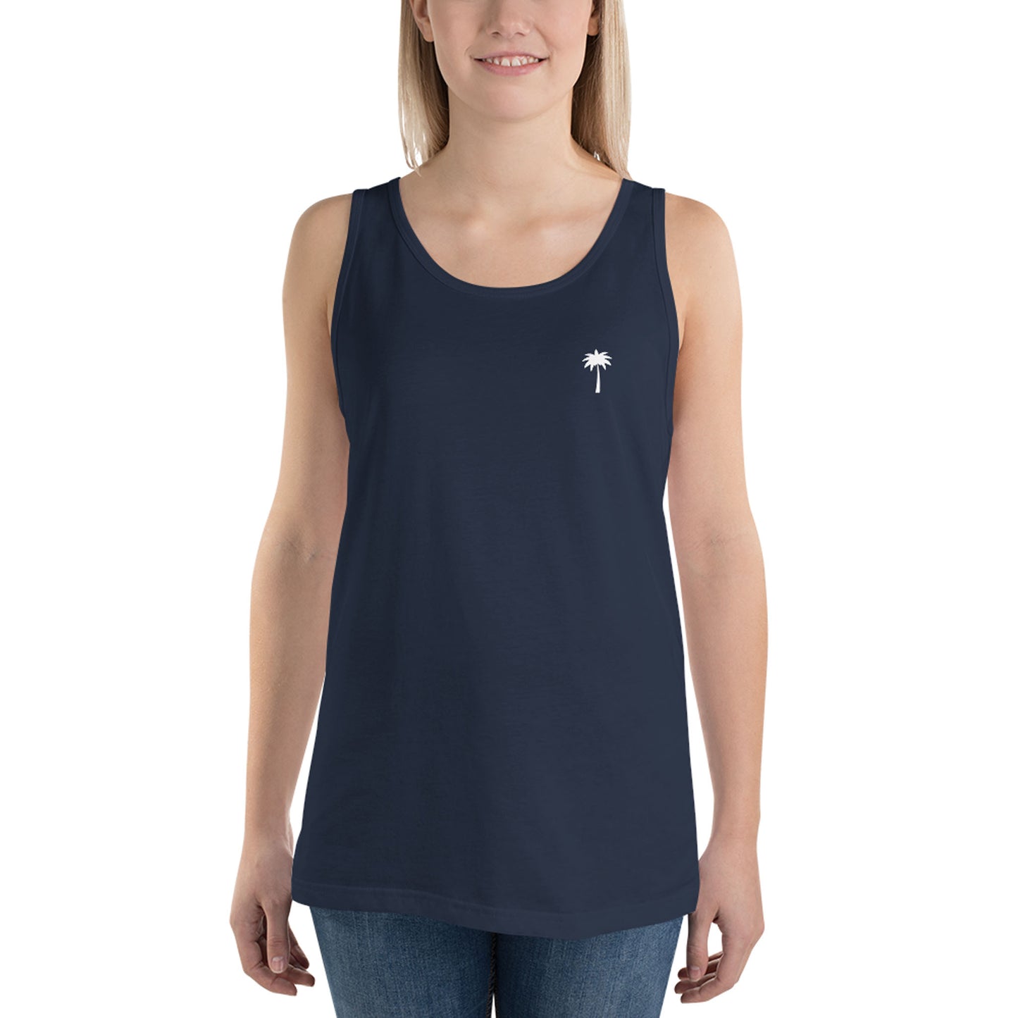 A woman wearing a sleeveless navy blue classic tank top made from ringspun cotton, featuring a small white palm tree graphic on the left chest, paired with blue jeans. She is smiling and facing forward.