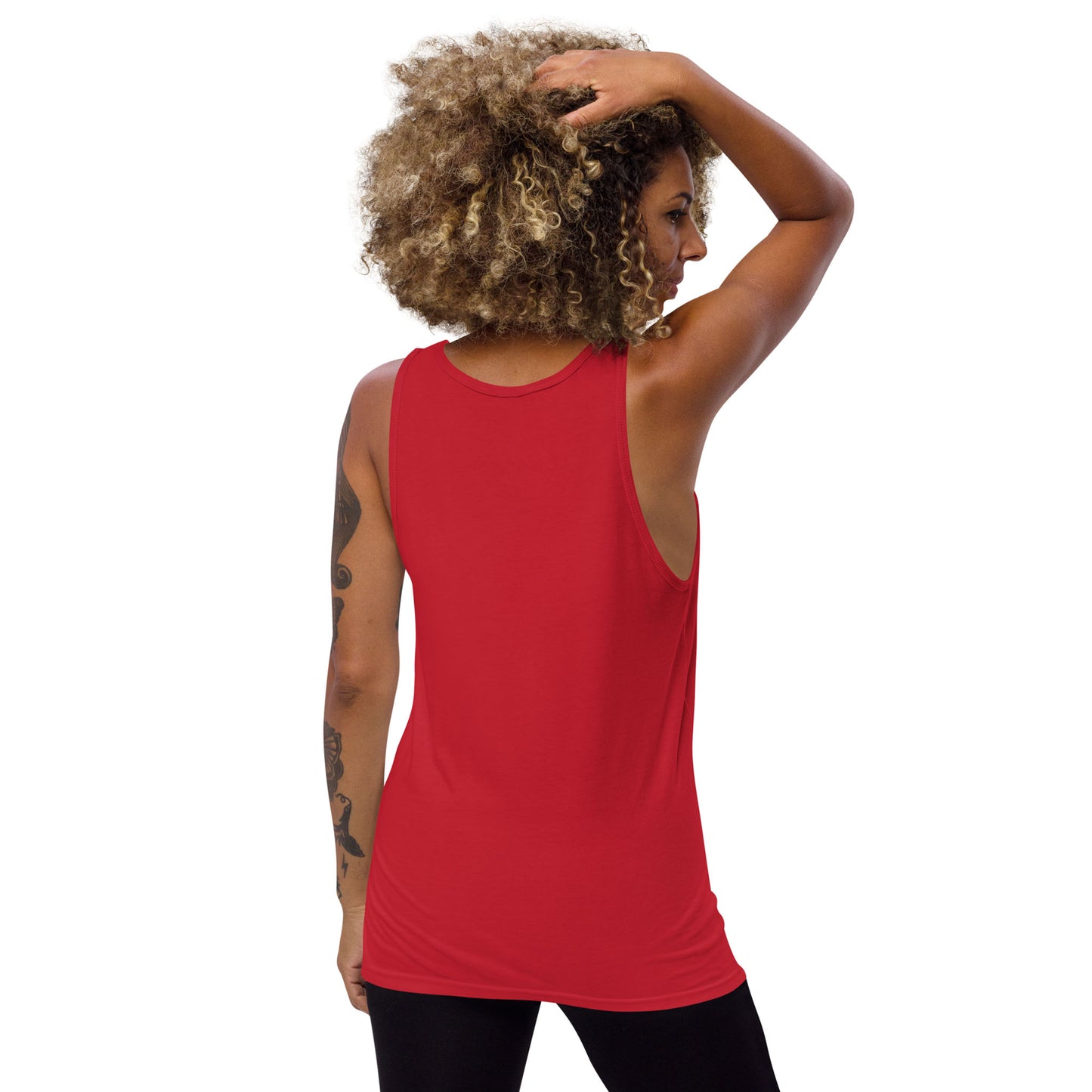 A person with curly hair and tattoos on their left arm stands with their back to the camera, wearing a sleeveless ringspun cotton classic tank top in red and black pants, one hand resting on their head against a plain white background.