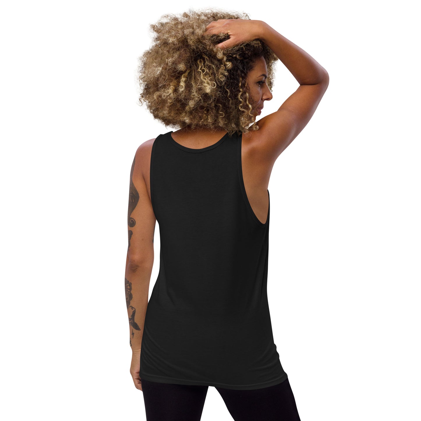 A person with curly hair and arm tattoos is shown from the back, wearing a loose black classic tank top and black leggings. They have one hand raised, touching their head. The background is plain white.