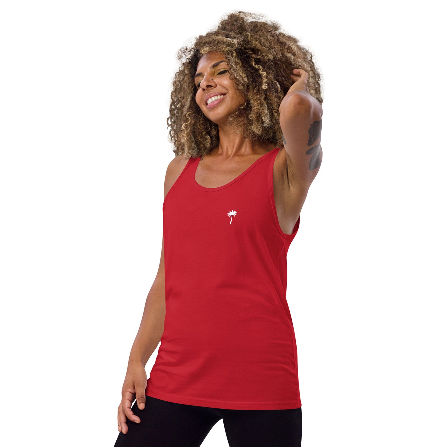 A smiling woman with curly hair wears a classic ringspun cotton tank top in red, featuring a small white palm tree graphic on the left chest, standing against a plain white background.