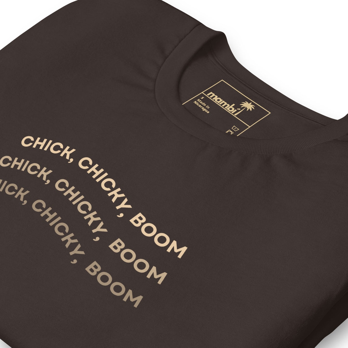 A folded black fitted shirt with the phrase CHICK, CHICKY, BOOM repeated three times in bold beige letters. Made from comfortable cotton, this graphic tee features a tan label inside the collar with branding details.
