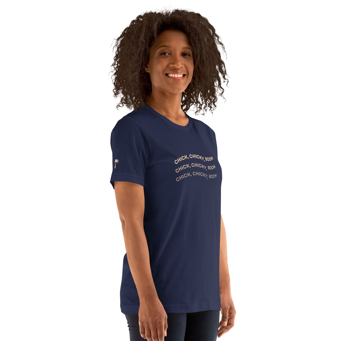 A woman with curly hair smiles as she stands slightly to the side, wearing a comfortable cotton navy blue fitted shirt that features “CHICK, CHICKY, BOOM” in white, set against a plain background.