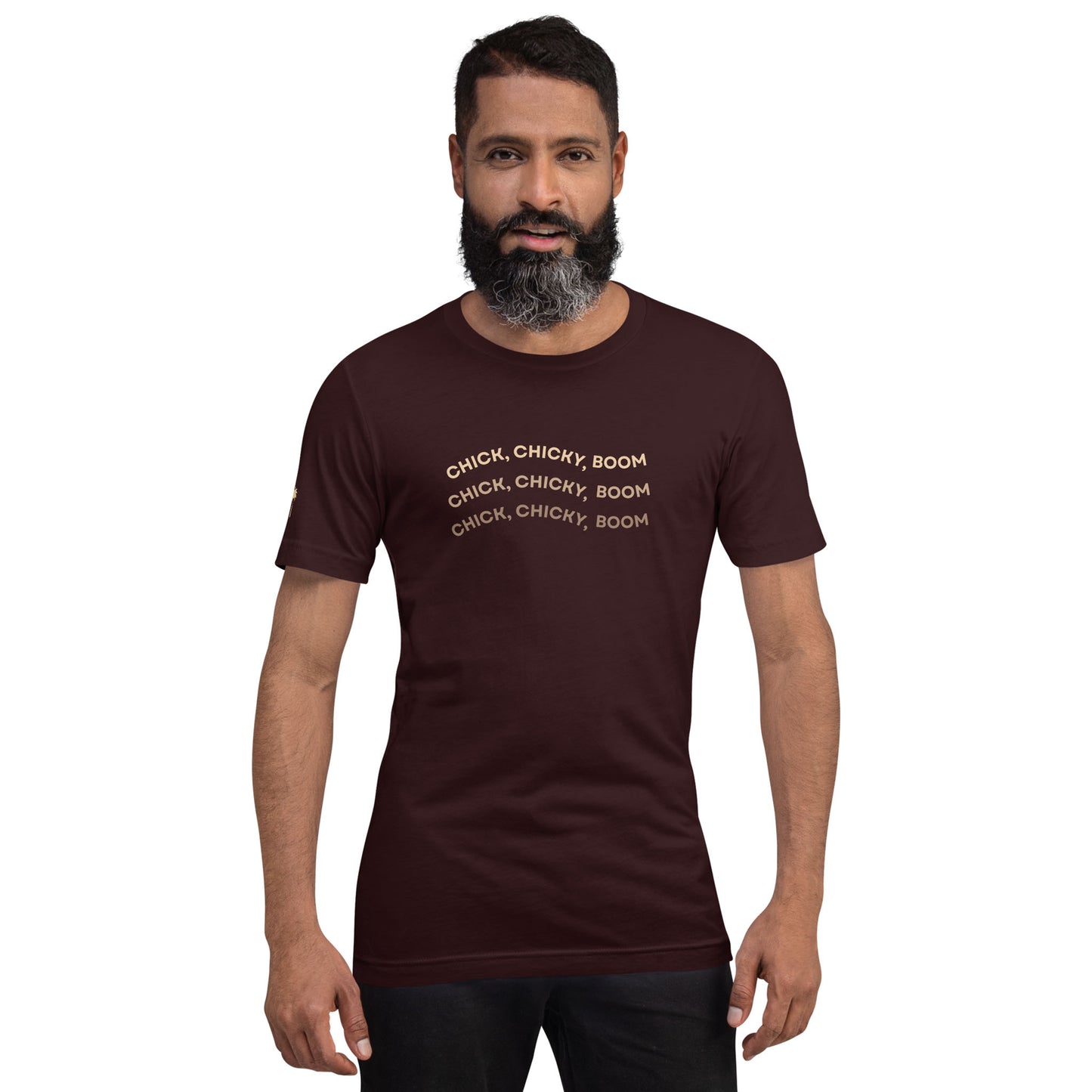 A bearded man with dark hair wears a fitted maroon graphic tee made of comfortable cotton, featuring the phrase “CHICK, CHICKY, BOOM” repeated three times in light-colored text, standing against a white background.