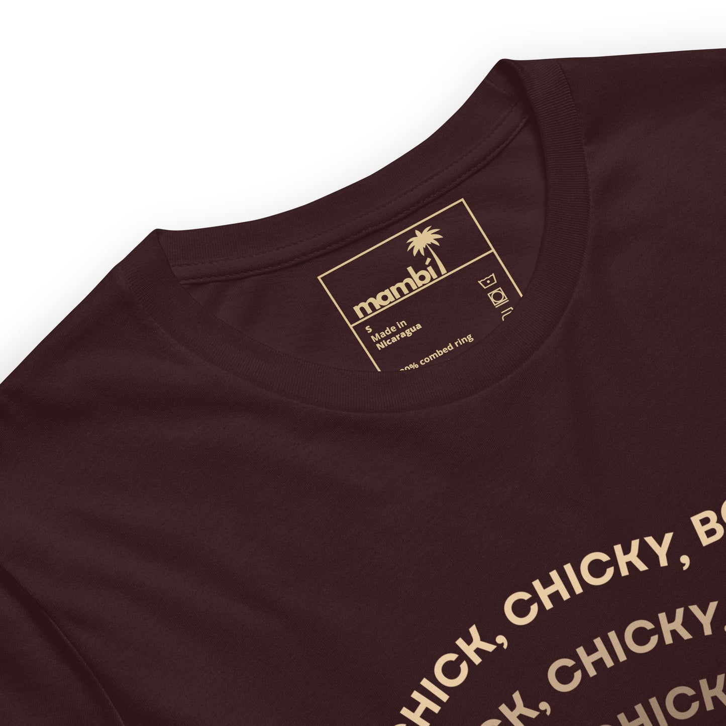 A close-up of a maroon fitted shirt in comfortable cotton with a printed inside label showing a palm tree, brand name mambi, and care instructions. Part of a gold text design is visible on the front, highlighting its graphic tees appeal.