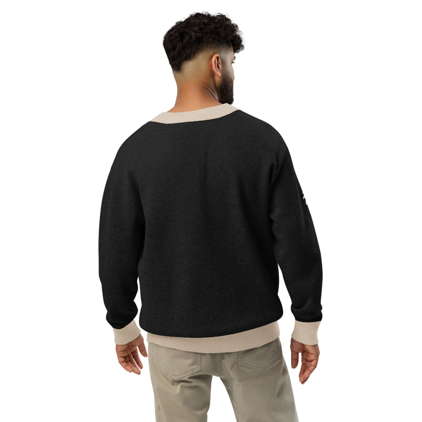 A man with short curly hair is standing with his back to the camera, wearing a two-tone cardigan with light beige cuffs and collar, paired with light-colored pants.