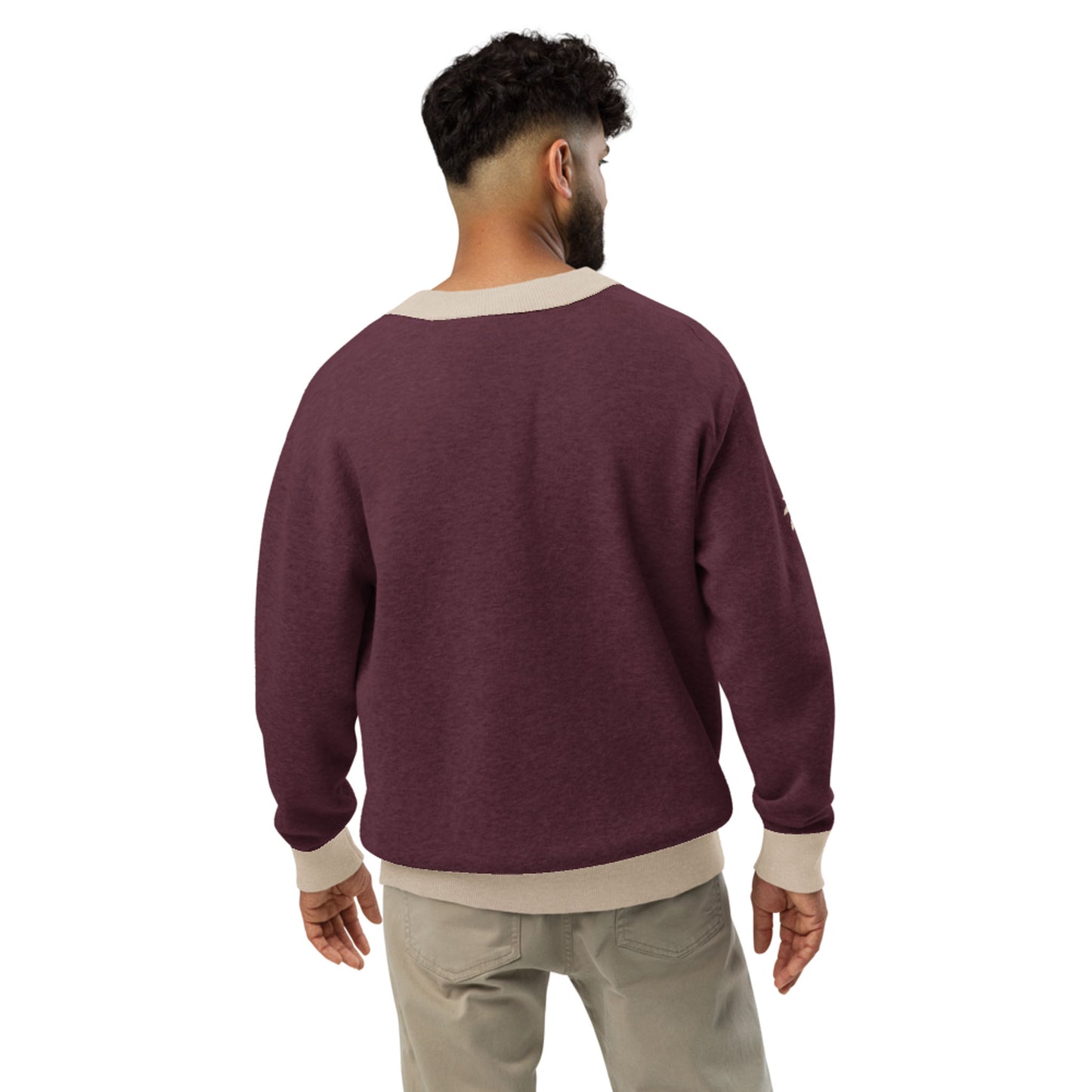 A man with short curly hair stands with his back to the camera, wearing a maroon jacquard knit cardigan with beige trim and light beige pants, set against a plain white background.