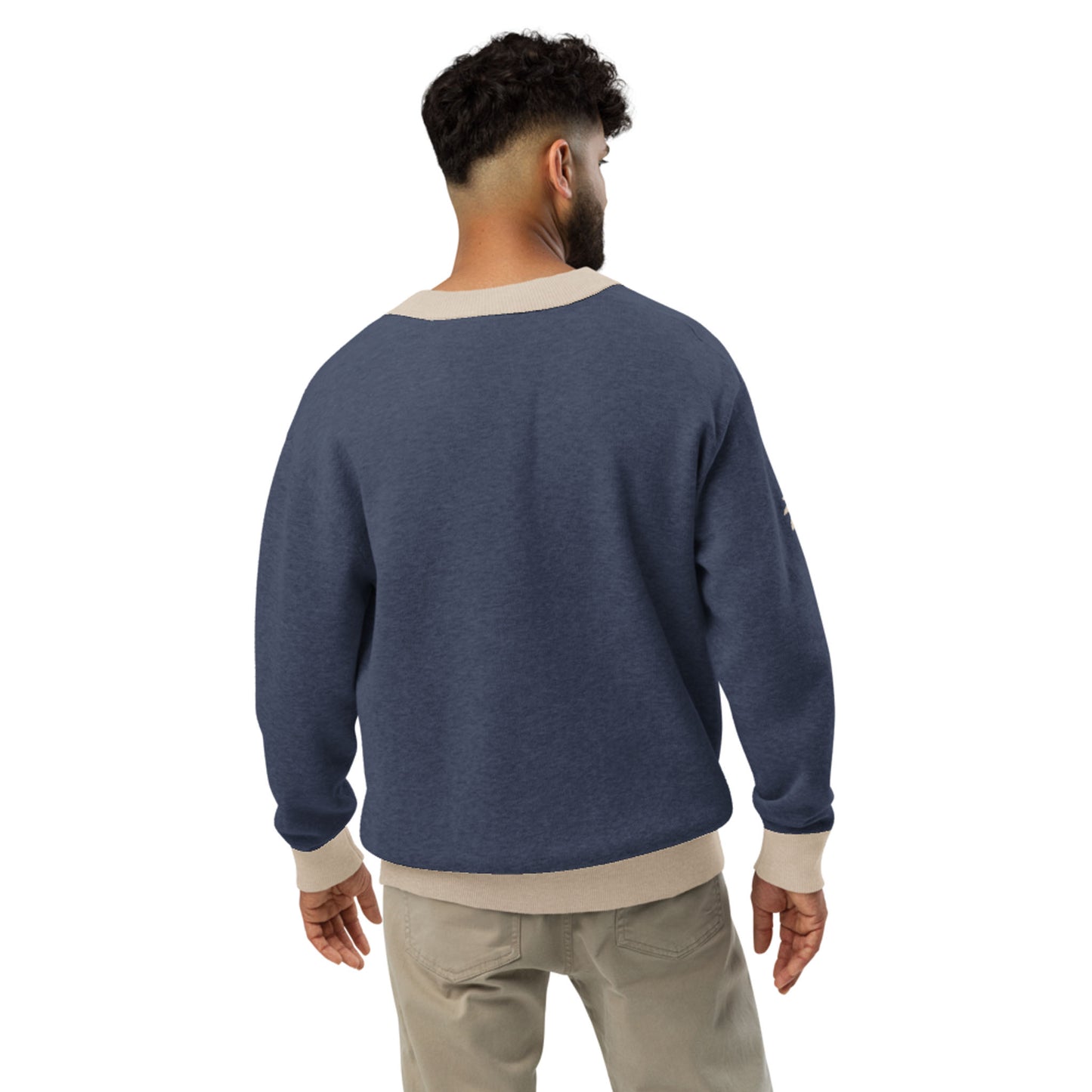 A man with short curly hair stands with his back to the camera, wearing a blue two-tone cardigan with a beige collar, cuffs, and hem, paired with light-colored pants. The background is plain white.
