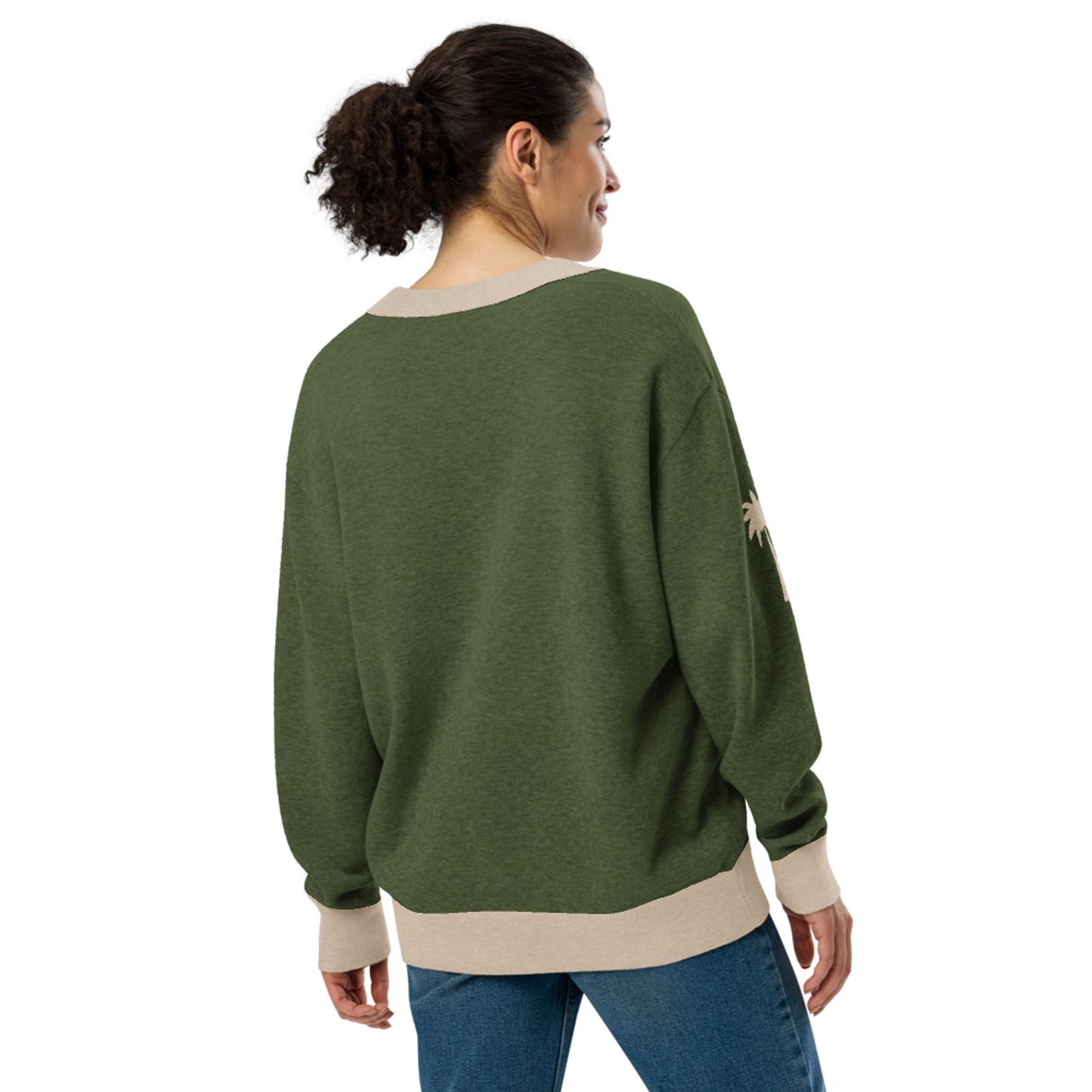 A woman with curly hair in a ponytail is standing and facing away. She is wearing a loose, two-tone cardigan with beige cuffs and hem, paired with blue jeans against a plain white background.