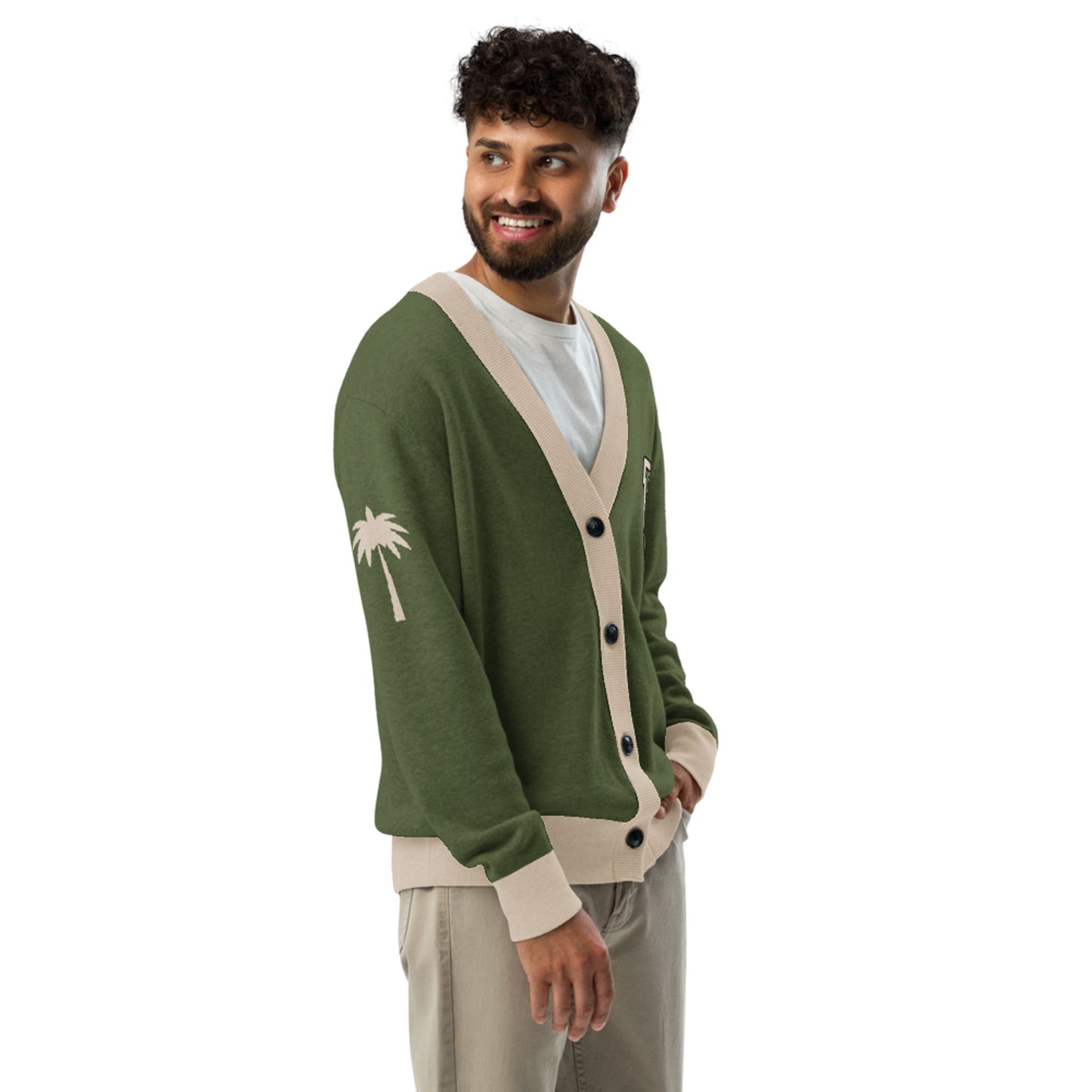 A man with curly hair and a beard smiles while wearing a unisex two-tone cardigan with beige trim, a white T-shirt, and beige pants. The jacquard knit cardigan features a white palm tree design on the sleeve.
