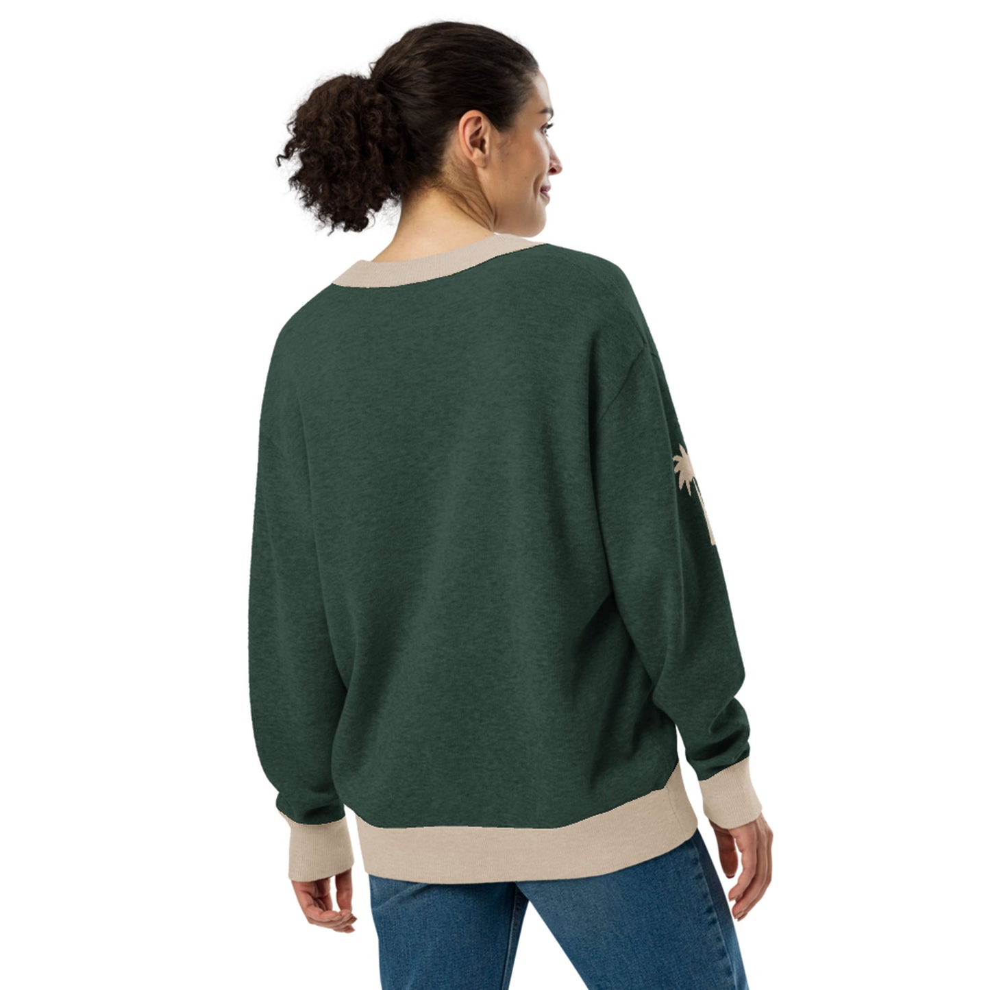 A woman with curly hair in a ponytail is wearing a two-tone cardigan with beige cuffs and hem, along with blue jeans. She is standing and facing away, looking slightly to the side.