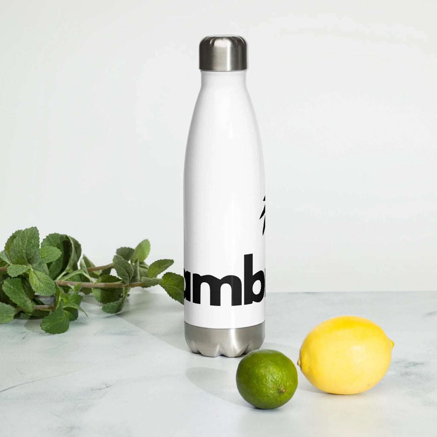 A Printful Pura Stainless Water Bottle, 17oz in white, stands on a marble surface with a lemon, lime, and mint. The double-walled bottle features bold black logo text against a plain, light background.