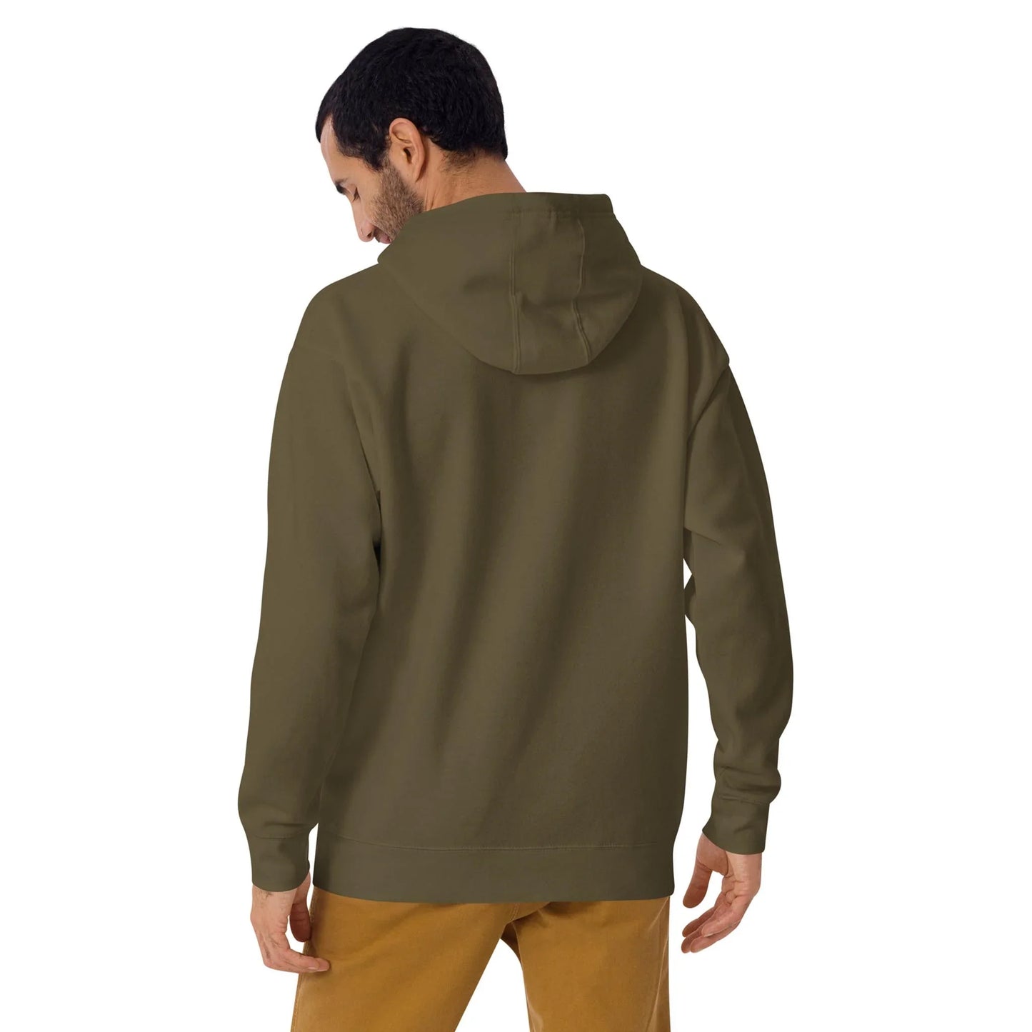 A man is standing with his back to the camera, wearing an olive green Mambí hooded sweatshirt and tan pants. His head is slightly turned to the left, and his right hand rests relaxed by his side.