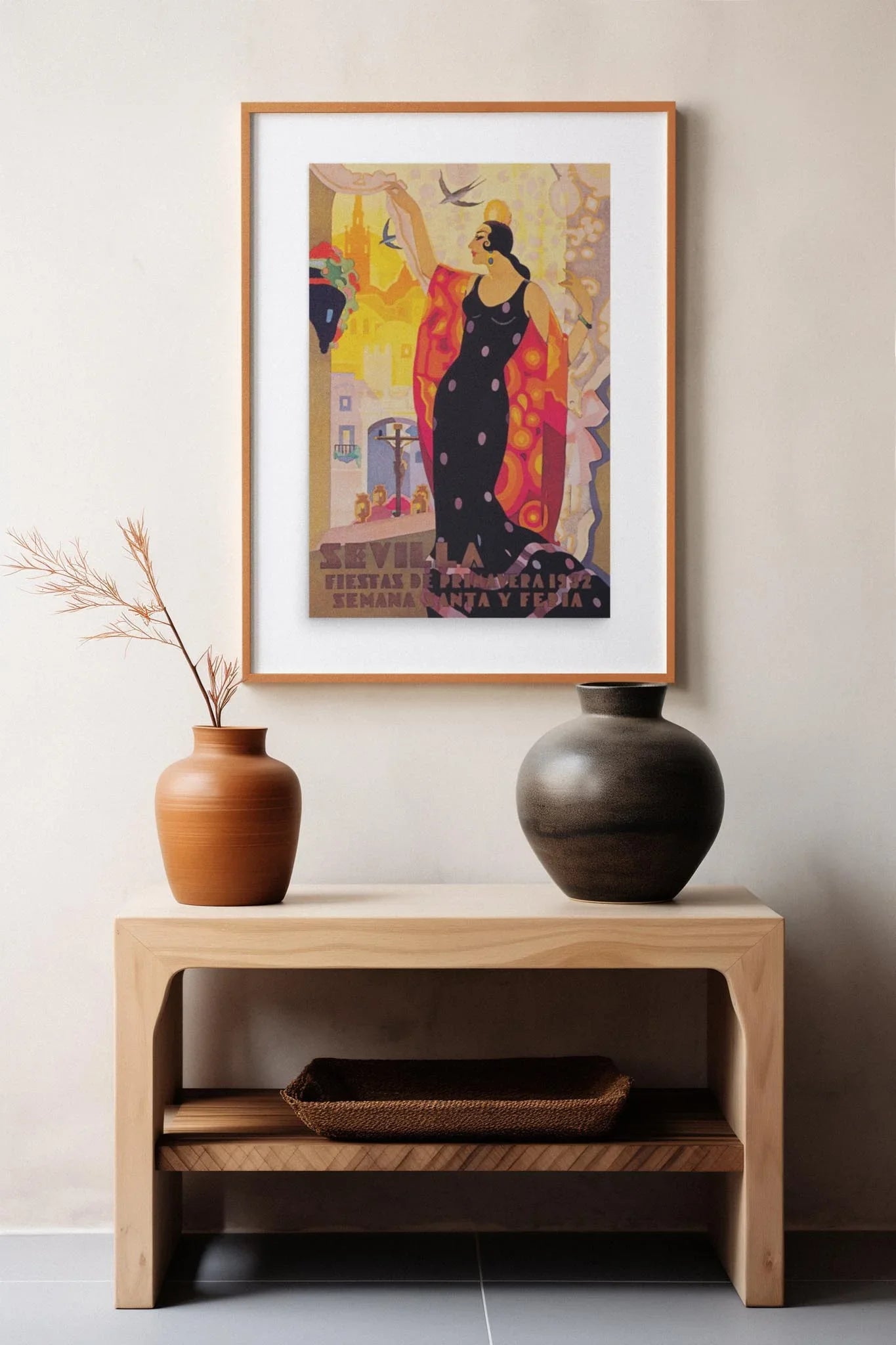 A wooden table with two ceramic vases and a basket sits by a light wall. Above hangs Printfuls Semana Santa y Feria de 1932 vintage poster (24x36, premium luster paper), showing a woman in red and festive Spanish city scene.
