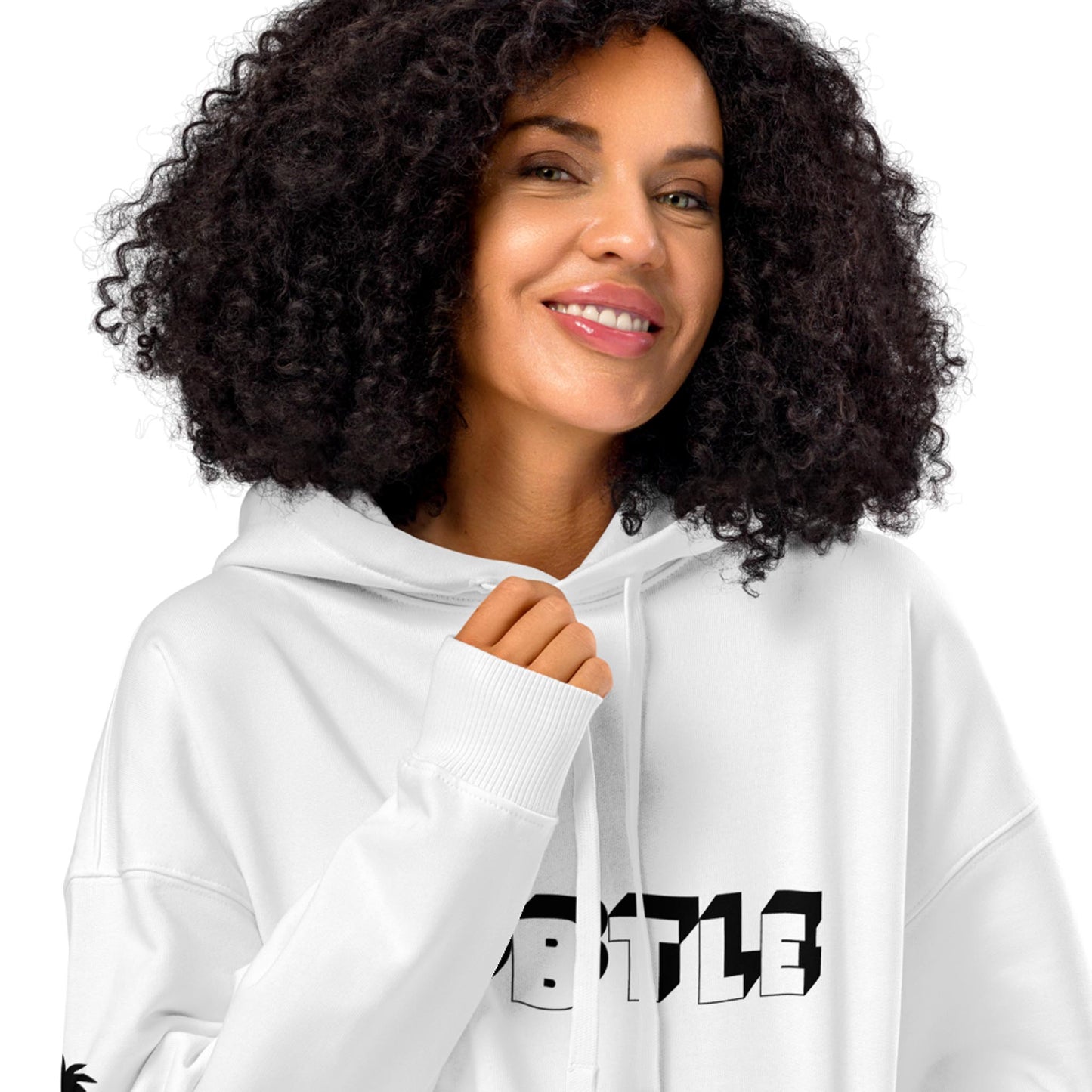 A woman with curly hair smiles while wearing a white Mambí hoodie with bold black text on the front. She holds one of the hoodie’s drawstrings, standing against a plain white background.