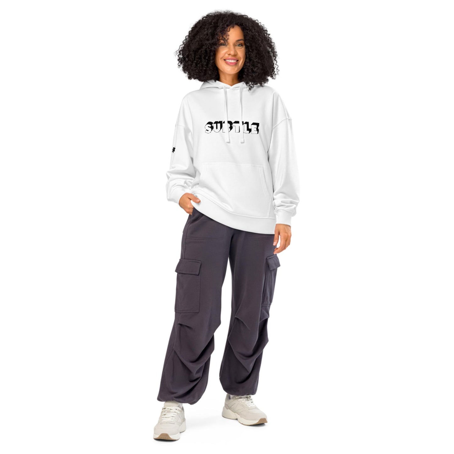 A person with curly hair wears a white Mambí hoodie with SWFL13 printed on it, dark cargo pants, and beige sneakers, standing and smiling against a white background.