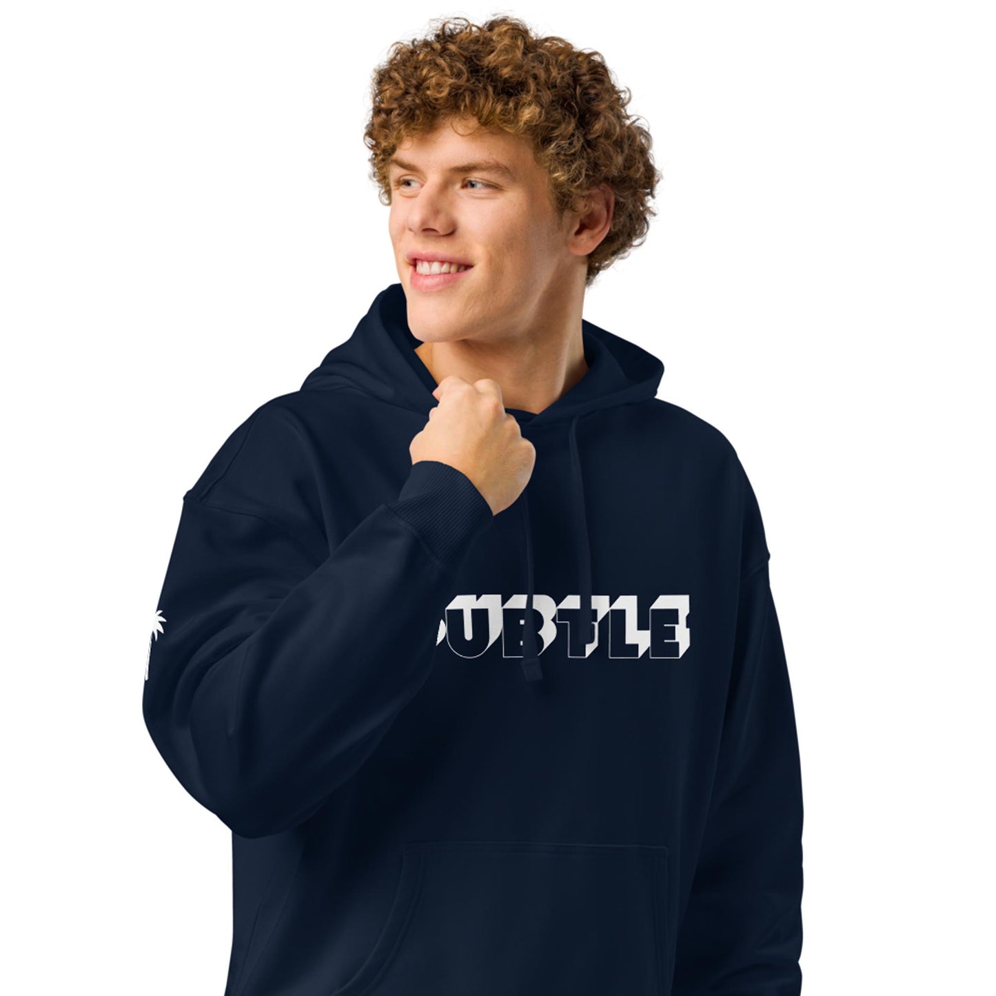 A person with curly hair, wearing a dark hoodie that says SUBTLE in bold white letters, smiles and looks to the side against a plain white background, embracing their unique Mambí style.