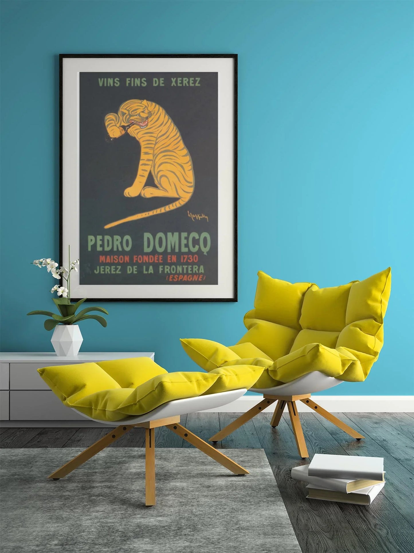 A modern room with turquoise walls, a yellow lounge chair and ottoman, a small white table with an orchid, books on the floor, and a framed vintage Mambí Pedro Domecq tiger poster on the wall.