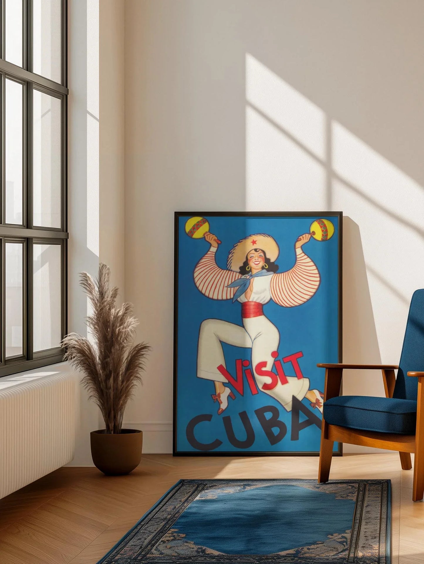 The Printful Visit Cuba Reprinted Vintage Poster (24x36, premium luster paper) is showcased in a sunlit room with wooden floors, a blue armchair, potted pampas grass, and a blue rug for an elegant touch.