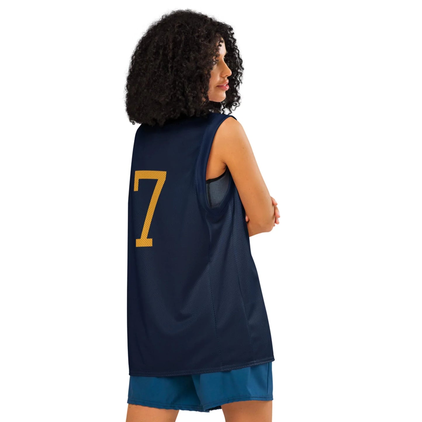 A woman with curly hair stands with arms crossed, wearing a navy Mambí sports jersey with the number 7 in yellow on the back and blue shorts, facing away from the camera.