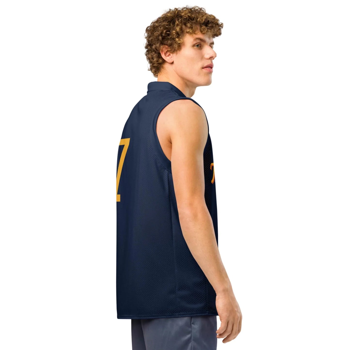 A young Mambí man with curly hair wears a sleeveless navy blue sports jersey with yellow numbers, standing sideways and looking over his shoulder.