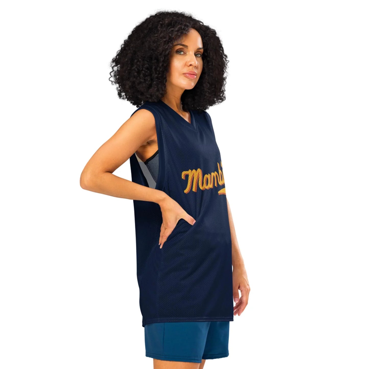 A woman with curly hair wears a sleeveless navy basketball jersey with Mambí in gold letters and teal shorts, standing with one hand in her pocket and facing slightly to the side.