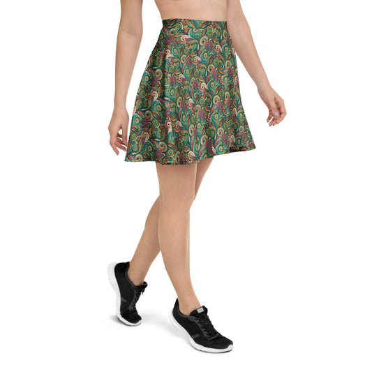 A woman wears the Printful Barbarita Skater Skirt, featuring a colorful paisley pattern with green, red, and orange swirls and an elastic waistband. Paired with black sneakers, she walks forward; only her lower half is visible.