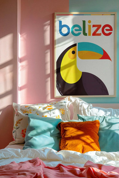 A cozy bed with colorful pillows and a floral pillowcase sits against a pink wall. Above the bed is a framed Mambí poster of a toucan and the word belize in bright colors. Sunlight streams in, casting shadows on the wall.