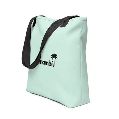 A light pastel green tote bag with black straps, featuring a black palm tree graphic and the word Mambí on the front. The tote stands upright at an angle against a white background.
