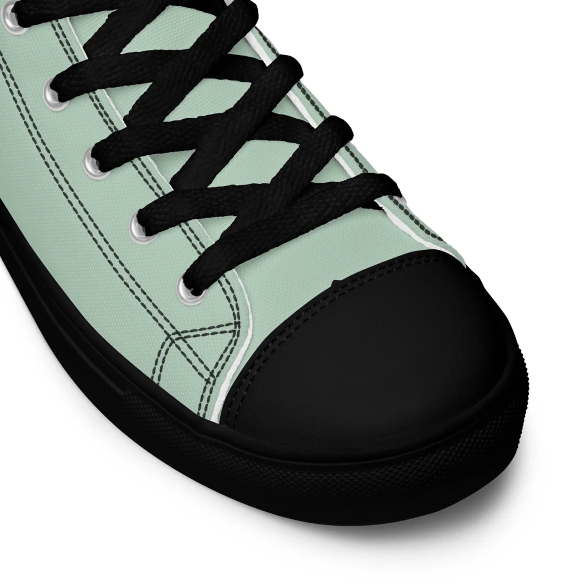 A close-up view of a light green Mambí canvas sneaker with black laces, black rubber toe cap, and black sole, showing detailed stitching and eyelets.