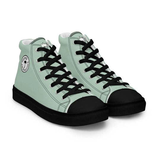A pair of light green high-top Mambí sneakers with black laces, black toe caps, and black soles. The shoes feature a circular white logo with black text and a star design on the ankle area.