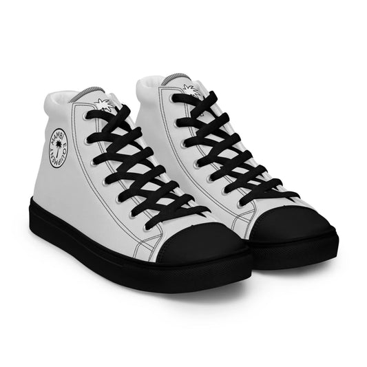 A pair of Mambí white high-top sneakers with black laces, soles, and toe caps. Each shoe features a circular logo with text and a palm tree graphic on the outer side near the ankle.