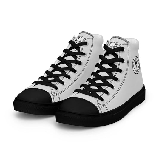 A pair of high-top sneakers with white uppers, black laces, black soles, and black toe caps. The tongue and side feature circular Mambí logos with text and a palm tree graphic.