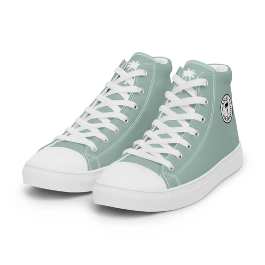 A pair of light green Mambí high-top sneakers with white laces, white soles, and a white round logo featuring palm trees on the side near the ankle.