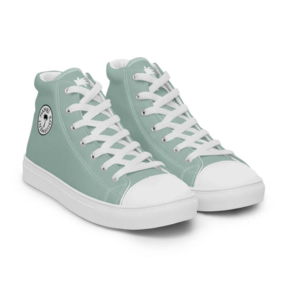 A pair of light teal Mambí high-top sneakers with white laces, white soles, and a circular black and white logo on the ankle area.