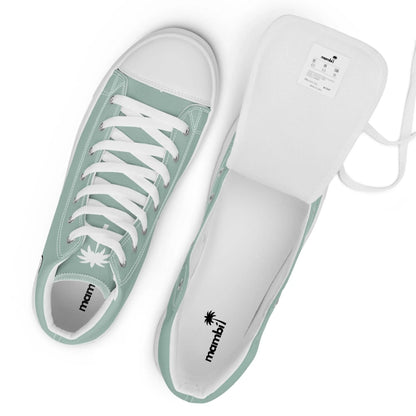 A pair of mint green Mambí low-top sneakers with white laces, white rubber toe caps, and white interiors. One shoe stands upright while the other rests on its side with the tongue pulled out to reveal the label.