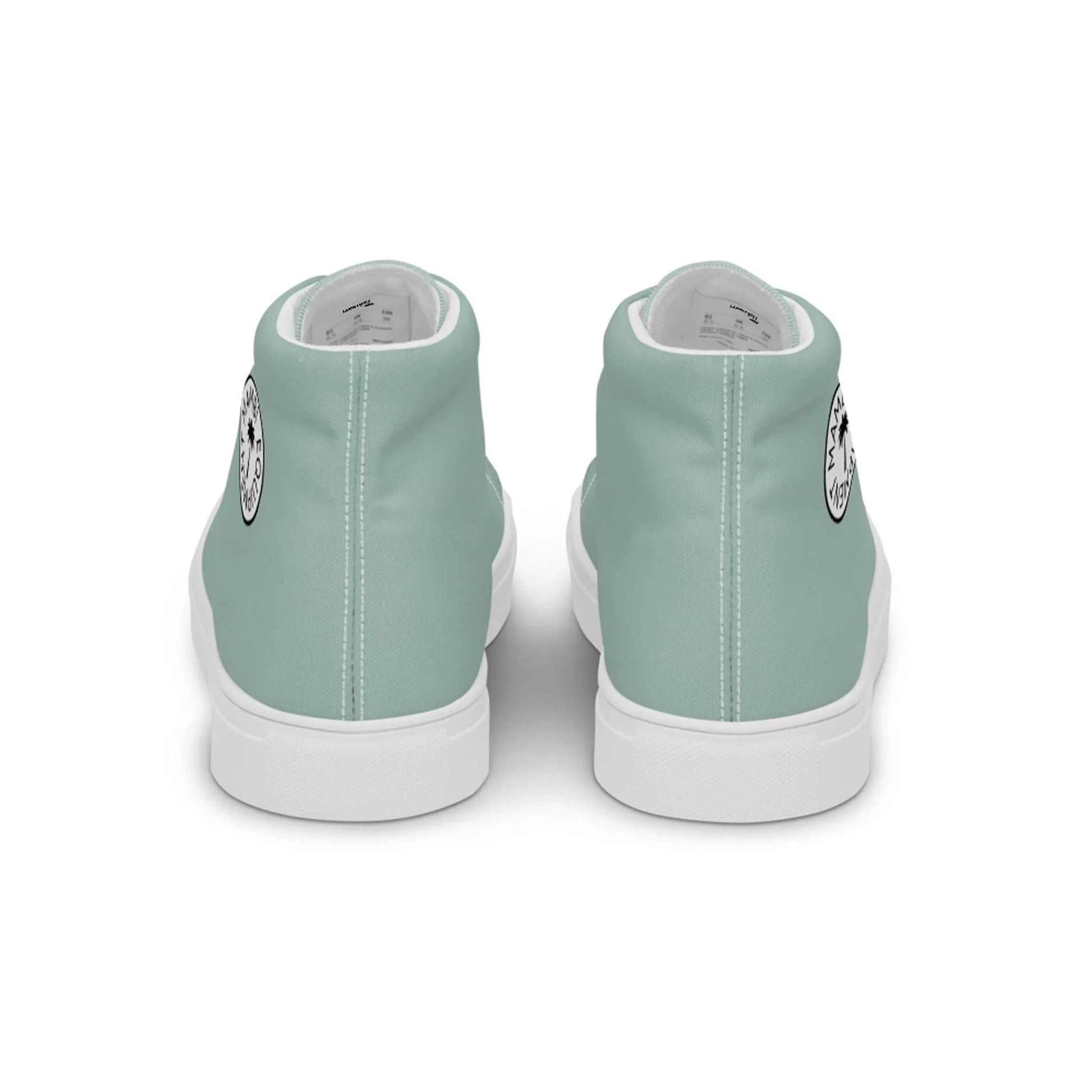 A pair of light teal Mambí high-top sneakers viewed from the back. Each shoe has a white sole and features a small circular black and white graphic on the outer side near the heel.