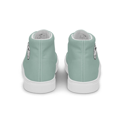 A pair of light teal Mambí high-top sneakers viewed from the back. Each shoe has a white sole and features a small circular black and white graphic on the outer side near the heel.