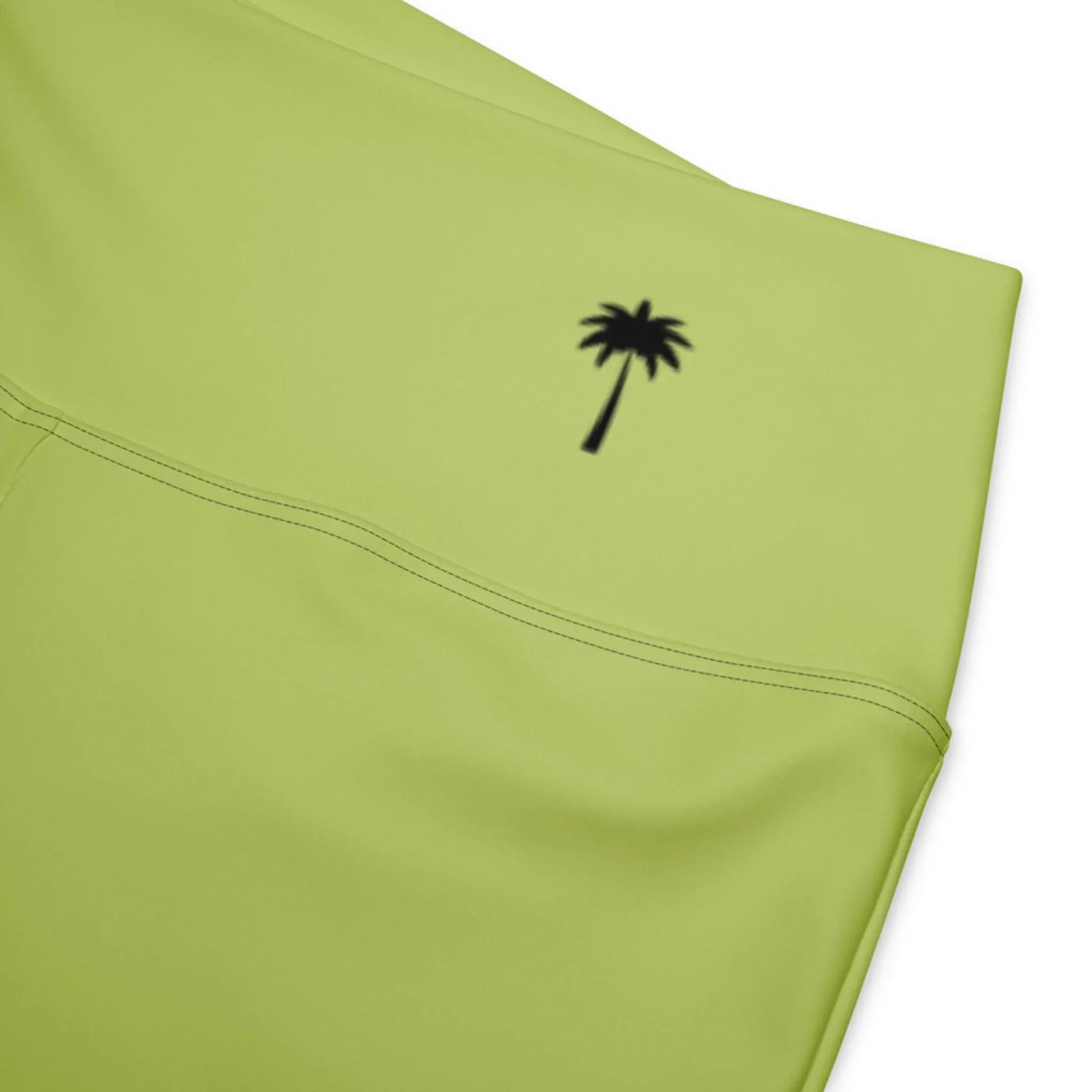 Close-up of light green Carolina Flared Performance Leggings by Printful, featuring a small black palm tree graphic near the waistband.