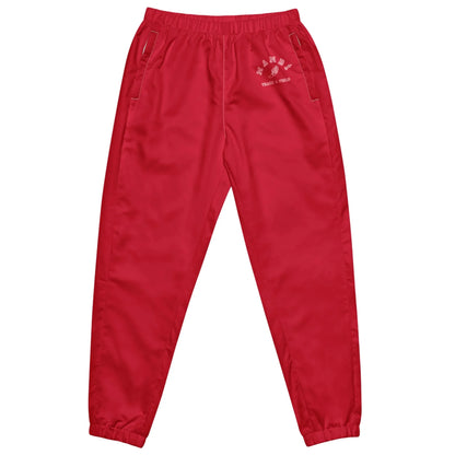 Bright red Mambí jogger pants with an elastic waistband, side pockets, and elastic cuffs at the ankles. A small white graphic and text accents the left hip area.