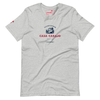 Light gray t-shirt with a blue and red graphic. Text reads: The Ultimate Destination CASA CARAJO above a cartoon-style house, adding a Mambí twist. Below, in small text: If you can find it. Red logo on left sleeve.