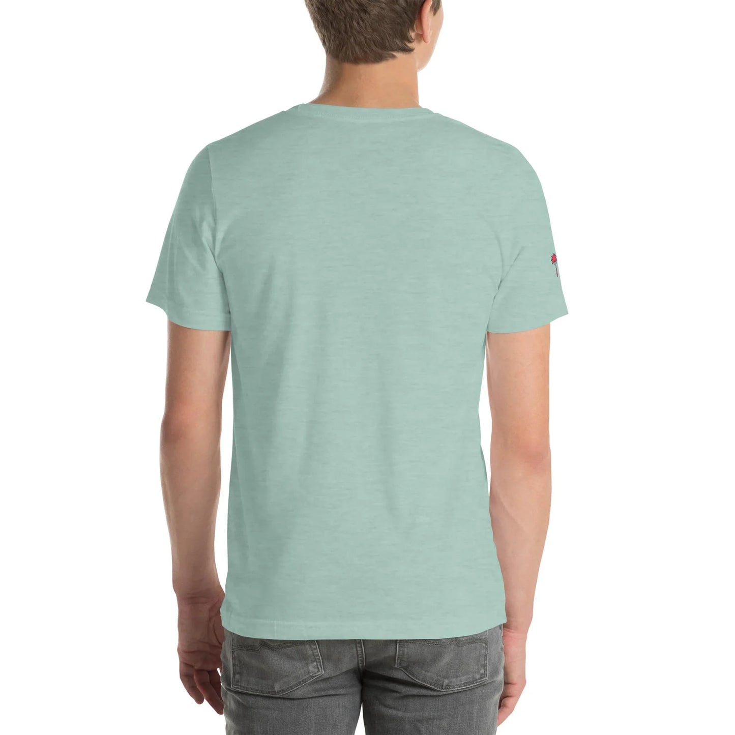 A person with short light brown hair is standing with their back to the camera, wearing a light mint green Mambí t-shirt and gray jeans against a plain white background.