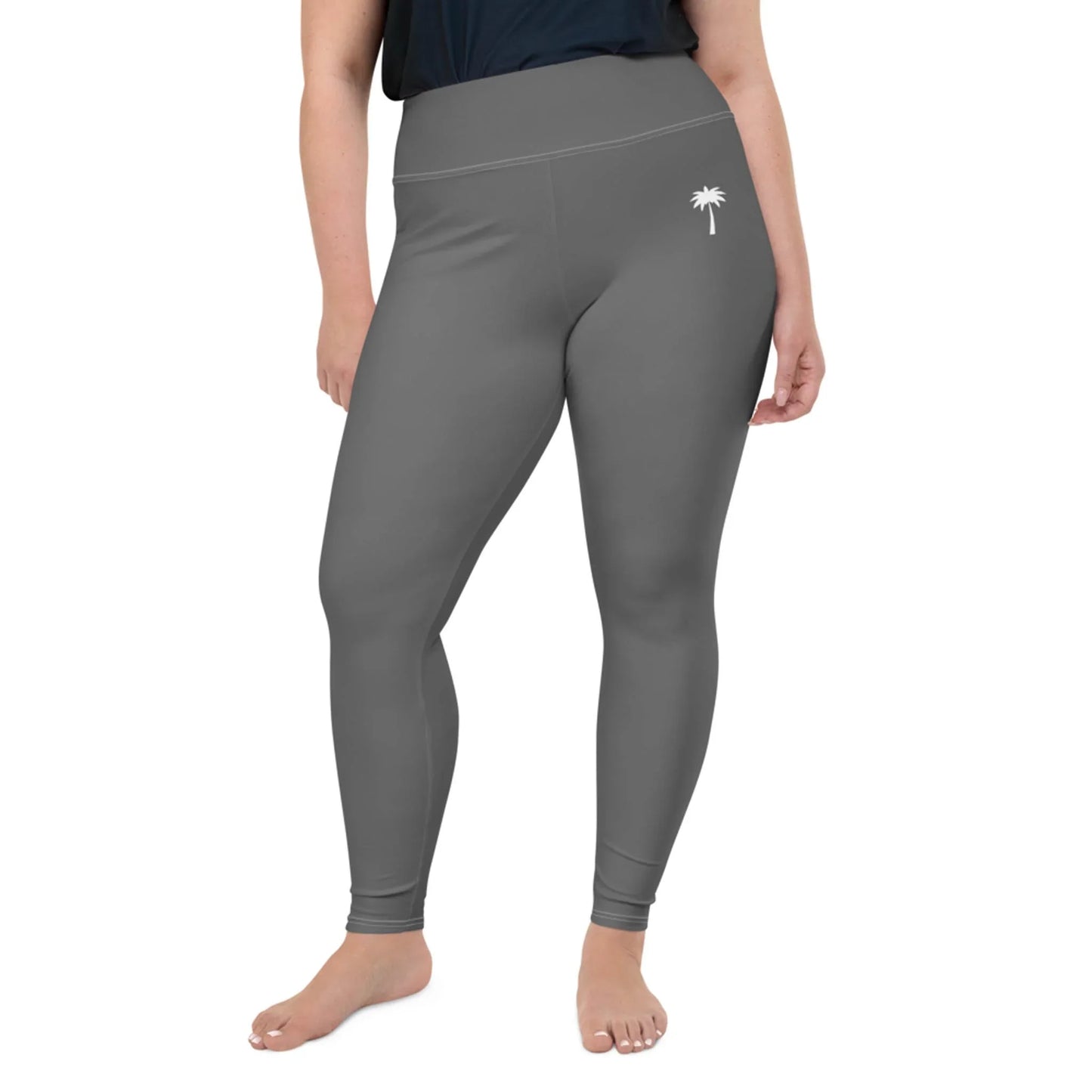 A person wearing high-waisted, gray Mambí leggings with a small white palm tree graphic on the left hip stands barefoot against a plain white background.
