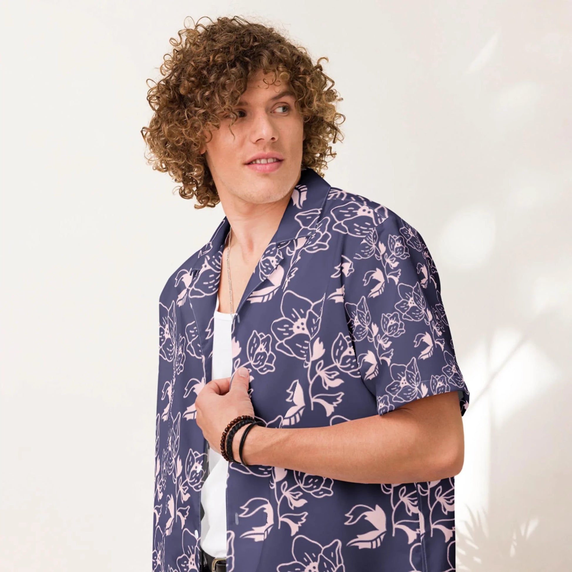 A person with curly hair wearing a navy blue Mambí shirt with a pink floral pattern over a white top, looking to the side against a light-colored background.