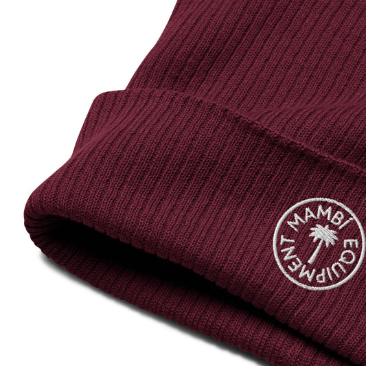 Close-up of a maroon ribbed knit beanie with a folded brim, featuring a white embroidered circular Mambí logo and palm tree design in the center.