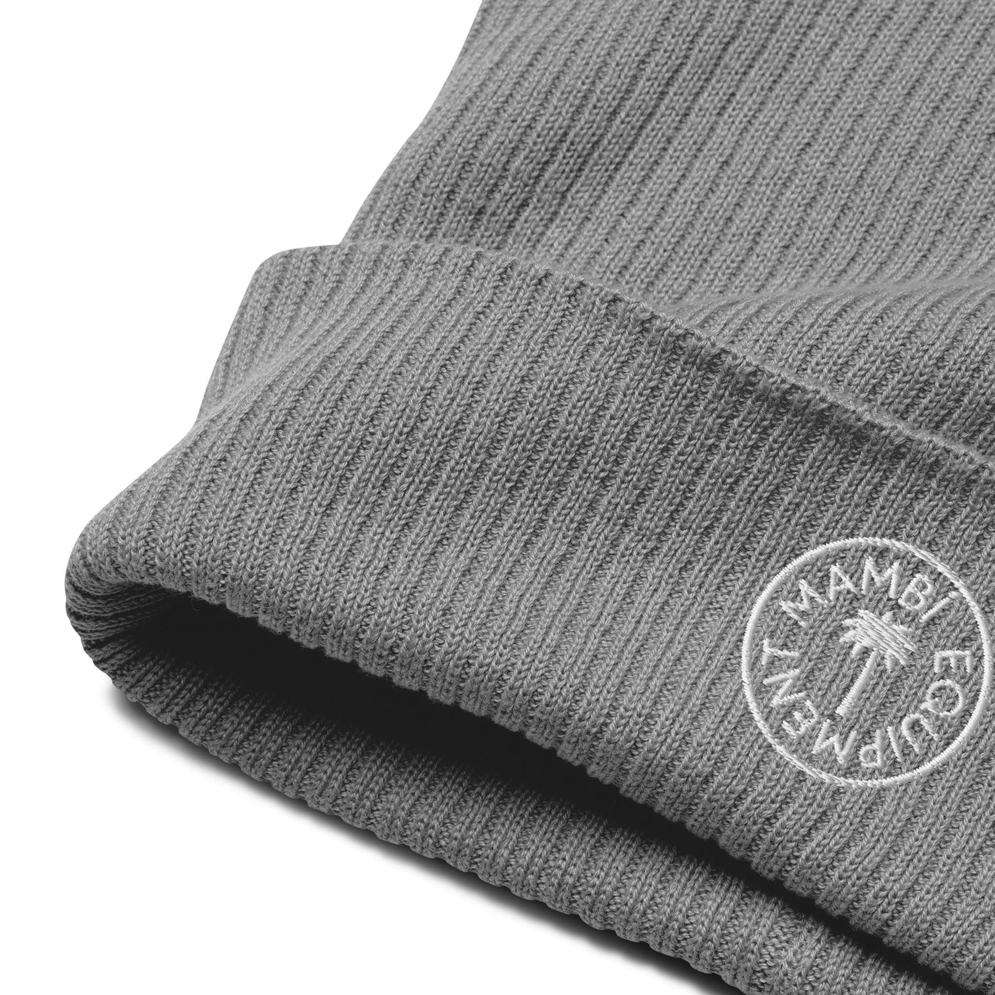 A close-up of a gray ribbed knit beanie featuring a white embroidered circular Mambí logo that reads ECOFRIENDLY around a palm tree graphic.