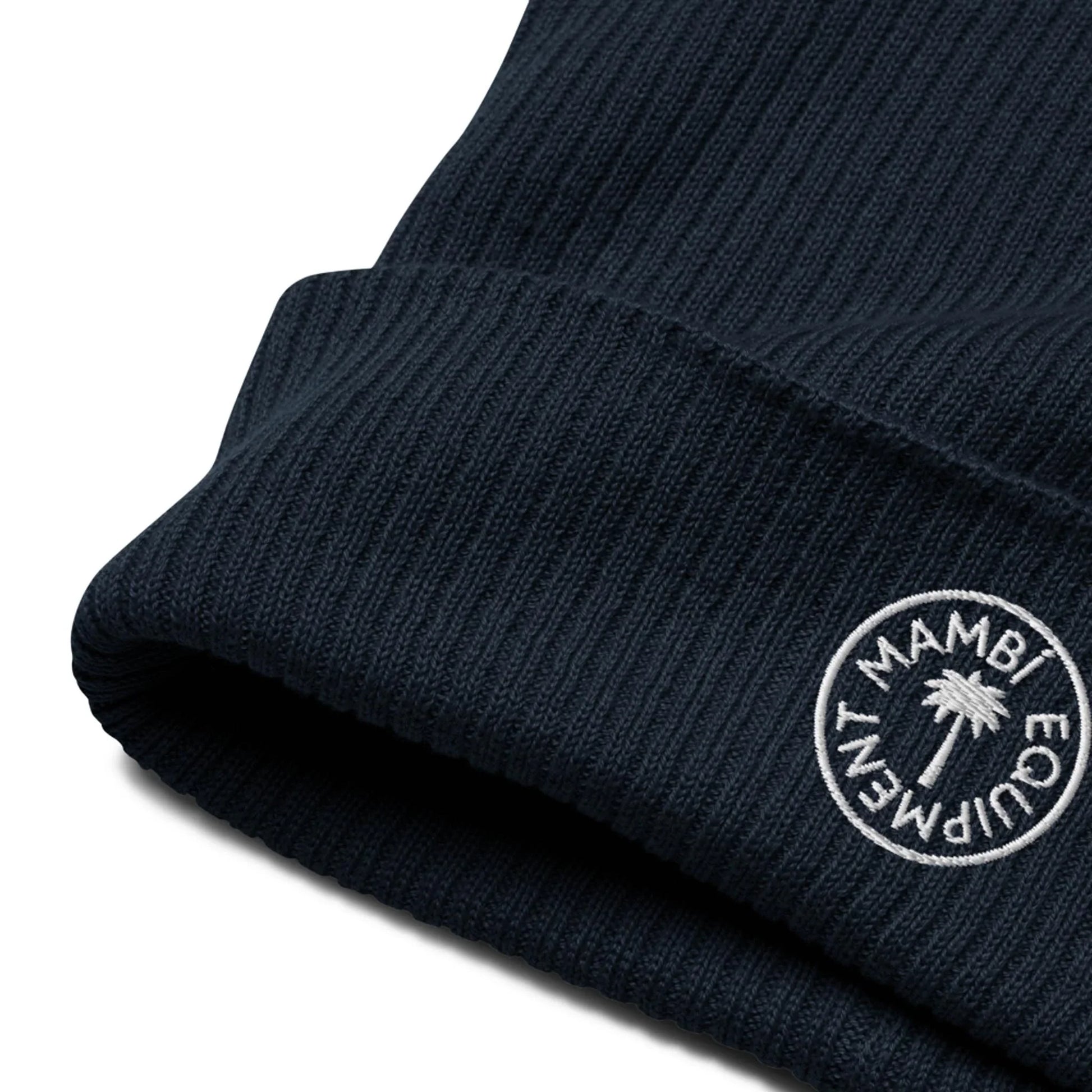 A close-up of a ribbed, dark navy knit beanie featuring a white circular patch with the text Mambí EQUIPMENT and a palm tree graphic embroidered on the cuff.